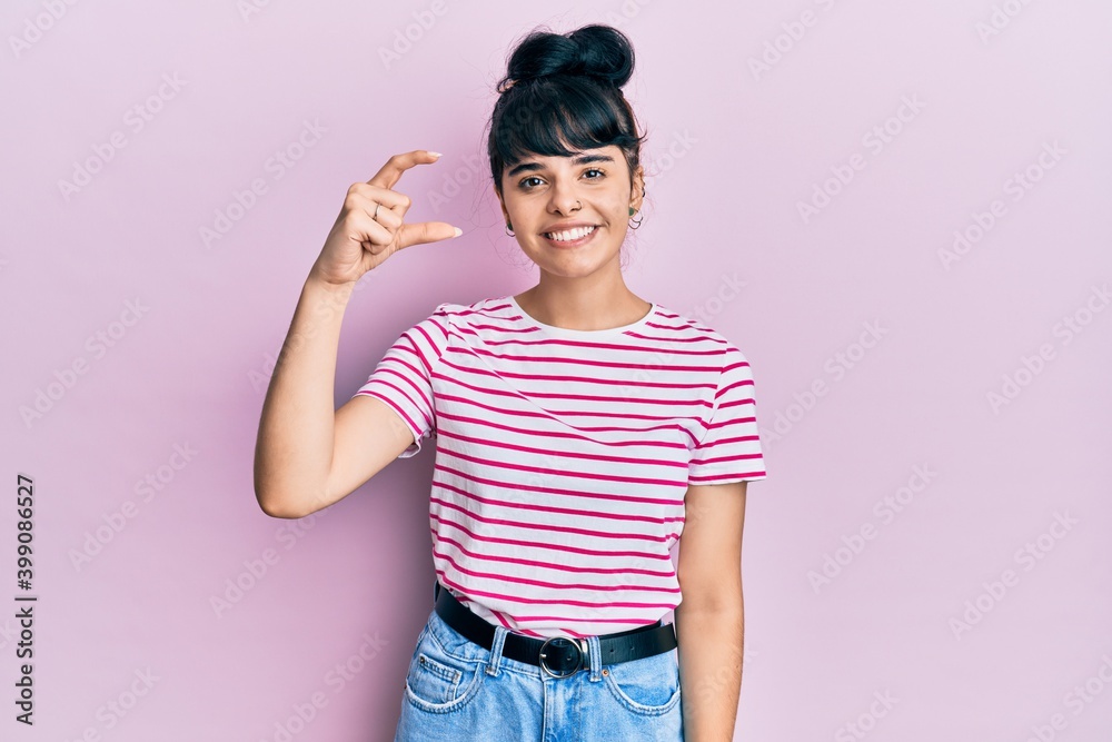 Young hispanic girl wearing casual clothes smiling and confident gesturing with hand doing small size sign with fingers looking and the camera. measure concept. Young hispanic girl wearing casual clothes smiling and confident gesturing with hand doing small size sign with fingers looking and the camera. measure concept.