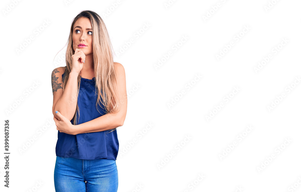 Young beautiful blonde woman wearing casual sleeveless t-shirt serious face thinking about question with hand on chin, thoughtful about confusing idea Young beautiful blonde woman wearing casual sleeveless t-shirt serious face thinking about question with hand on chin, thoughtful about confusing idea