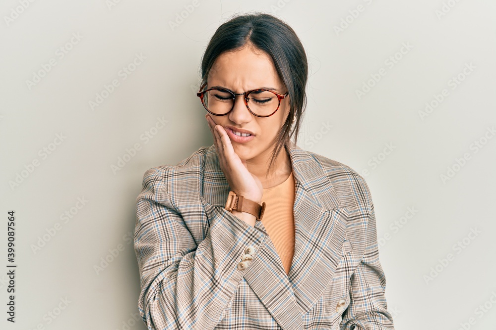 Young brunette woman wearing business jacket and glasses touching mouth with hand with painful expression because of toothache or dental illness on teeth. dentist Young brunette woman wearing business jacket and glasses touching mouth with hand with painful expression because of toothache or dental illness on teeth. dentist