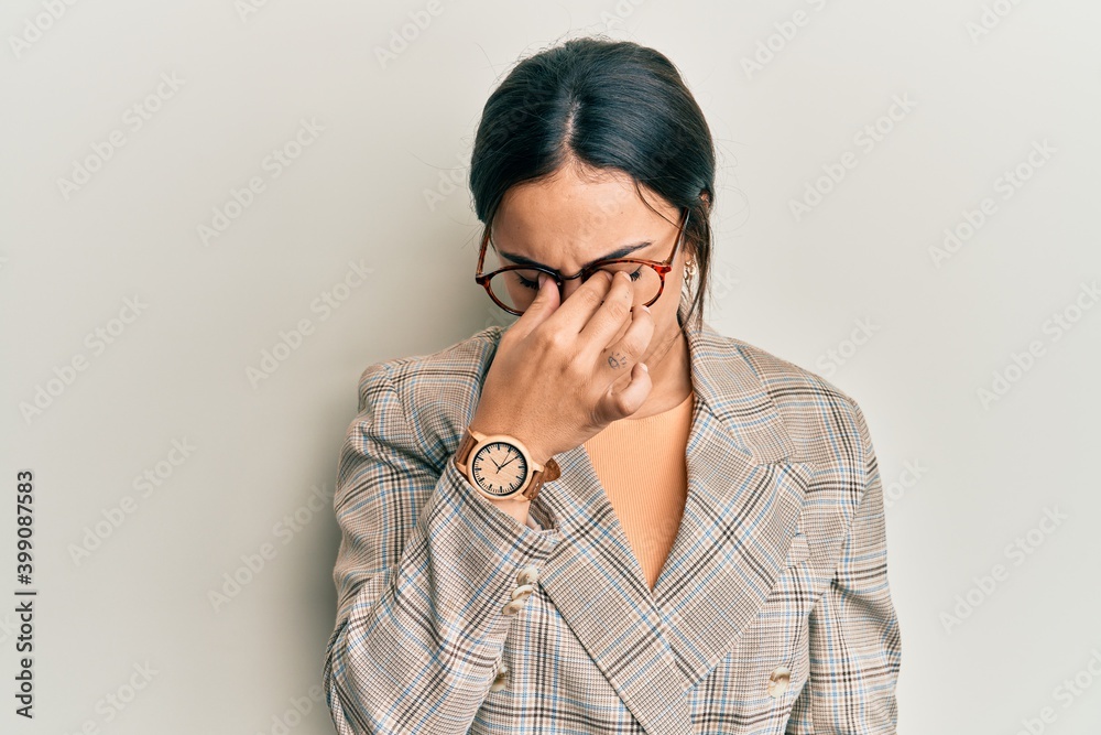 Young brunette woman wearing business jacket and glasses tired rubbing nose and eyes feeling fatigue and headache. stress and frustration concept. Young brunette woman wearing business jacket and glasses tired rubbing nose and eyes feeling fatigue and headache. stress and frustration concept.