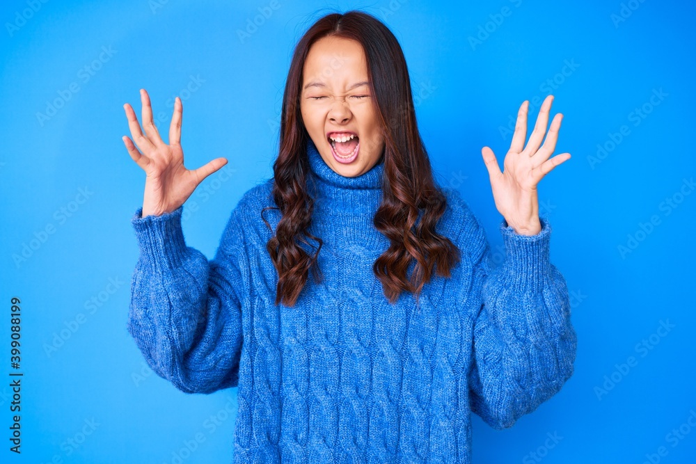 Young beautiful chinese girl wearing casual winter sweater celebrating mad and crazy for success with arms raised and closed eyes screaming excited. winner concept Young beautiful chinese girl wearing casual winter sweater celebrating mad and crazy for success with arms raised and closed eyes screaming excited. winner concept