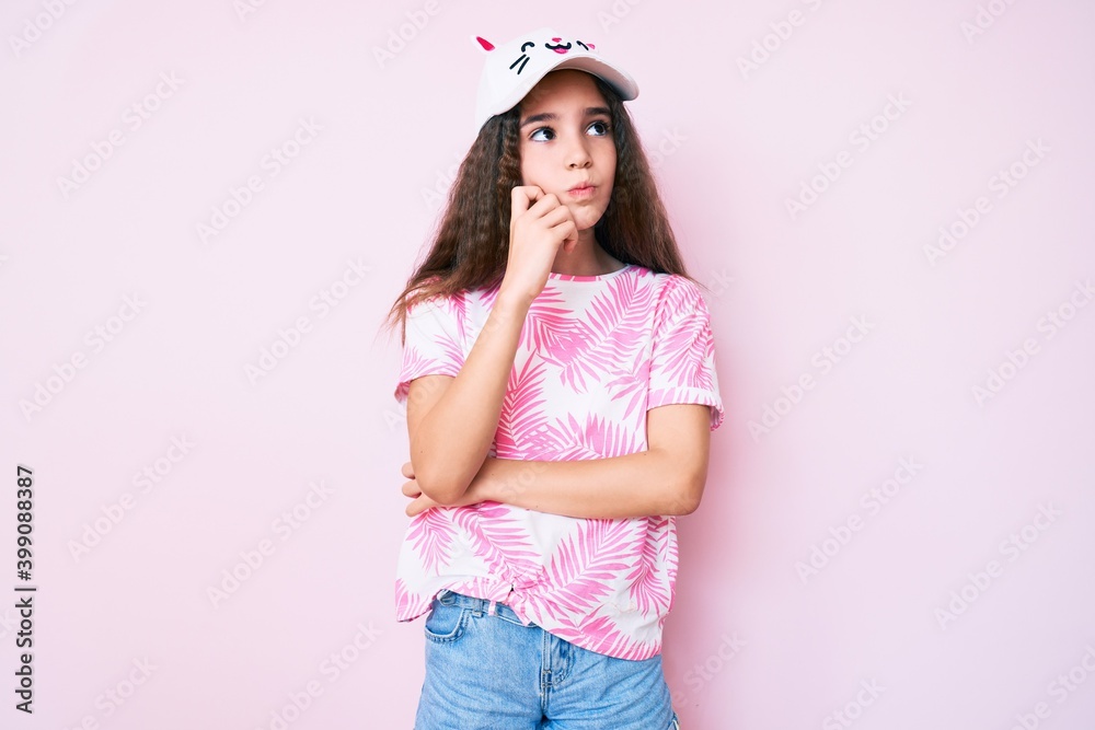 Cute hispanic child girl wearing casual clothes and funny kitty cap serious face thinking about question with hand on chin, thoughtful about confusing idea Cute hispanic child girl wearing casual clothes and funny kitty cap serious face thinking about question with hand on chin, thoughtful about confusing idea