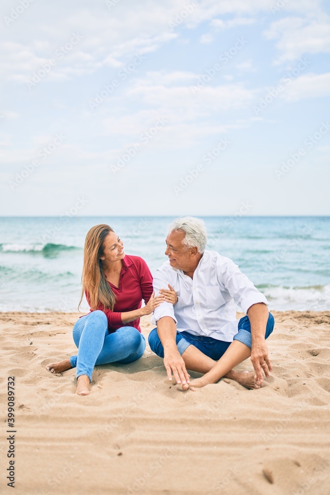 Middle age hispanic couple smiling happy and hugging sitting at the beach Middle age hispanic couple smiling happy and hugging sitting at the beach