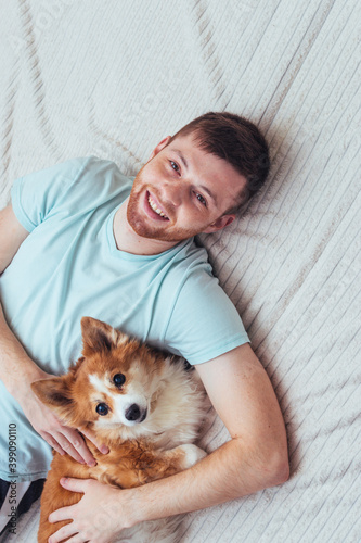 Young handsome man lies in an embrace with a ginger dog. Vertical photo