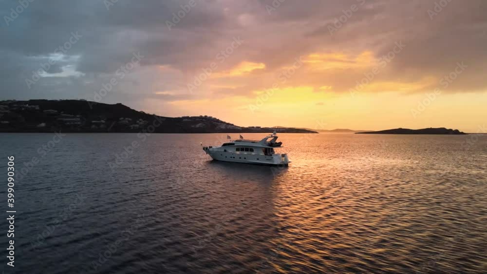 Aerial shot orbiting around a big yacht navigating near Mykonos island at sunset Aerial shot orbiting around a big yacht navigating near Mykonos island at sunset