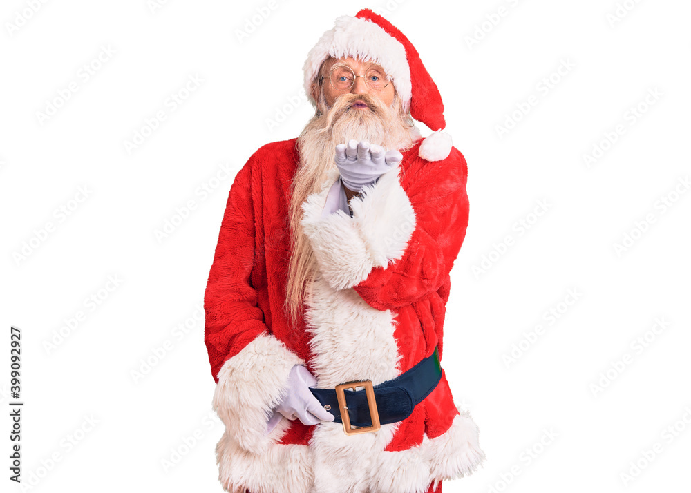 Old senior man with grey hair and long beard wearing traditional santa claus costume looking at the camera blowing a kiss with hand on air being lovely and sexy. love expression. Old senior man with grey hair and long beard wearing traditional santa claus costume looking at the camera blowing a kiss with hand on air being lovely and sexy. love expression.