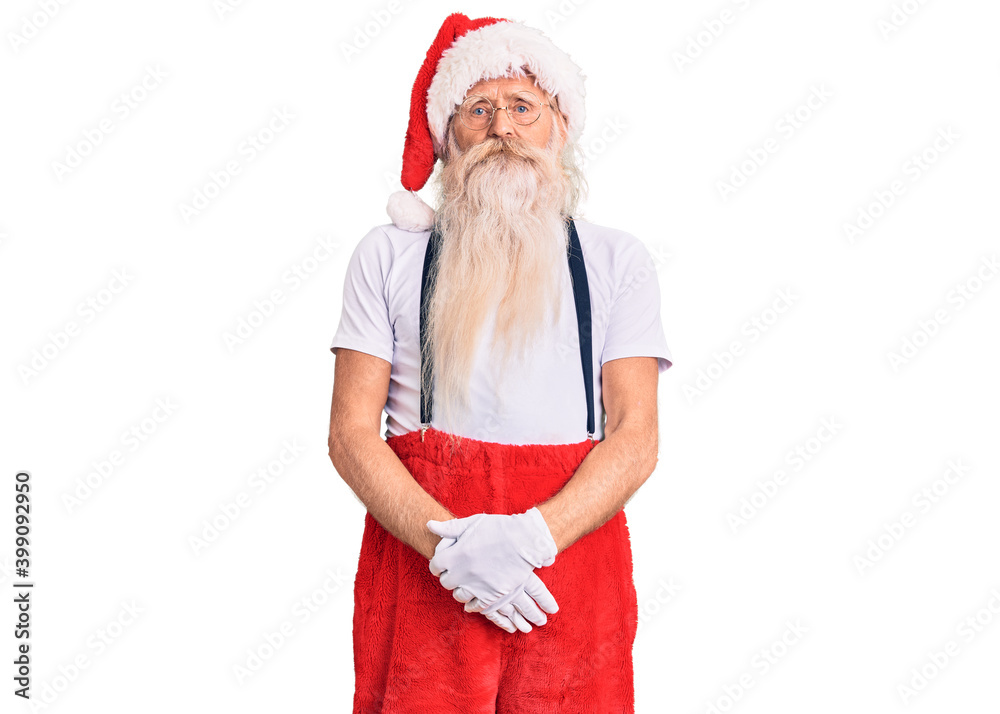 Obraz premium Old senior man with grey hair and long beard wearing santa claus costume with suspenders with serious expression on face. simple and natural looking at the camera.
