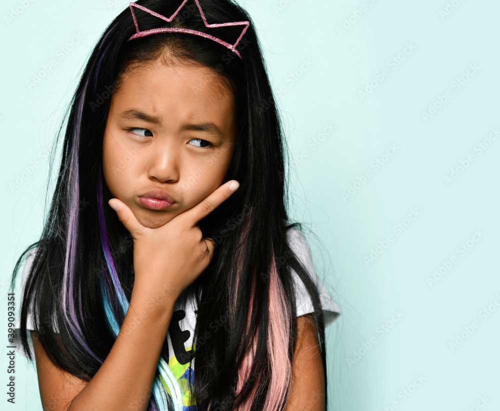 Close up portrait of capricious brunette girl in crown hoop and with colored strands in hair on blue background. Concept image for articles about children's tantrums and whims. Banner. Place for text. Close up portrait of capricious brunette girl in crown hoop and with colored strands in hair on blue background. Concept image for articles about children's tantrums and whims. Banner. Place for text.