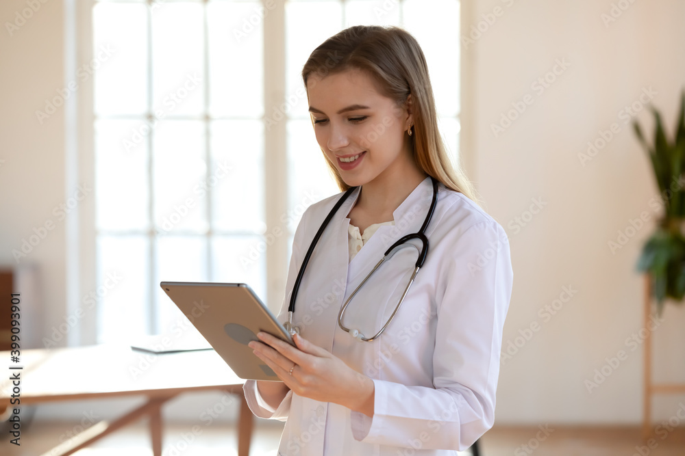 Smiling young Caucasian female doctor or nurse in white medical uniform look at tablet screen consult client online. Happy woman GP or physician use pad, have video call consultation with patient. Smiling young Caucasian female doctor or nurse in white medical uniform look at tablet screen consult client online. Happy woman GP or physician use pad, have video call consultation with patient.