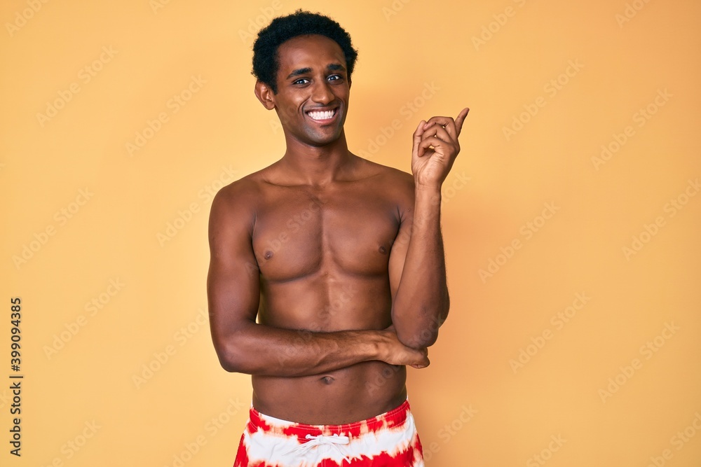 African handsome man wearing swimsuit smiling happy pointing with hand and finger to the side
