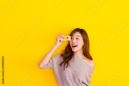 Cheerful Asian woman traveler posing for a photography on yellow background.