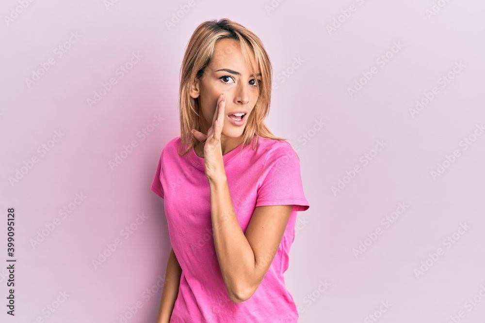 Beautiful blonde woman wearing casual pink tshirt hand on mouth telling secret rumor, whispering malicious talk conversation Beautiful blonde woman wearing casual pink tshirt hand on mouth telling secret rumor, whispering malicious talk conversation