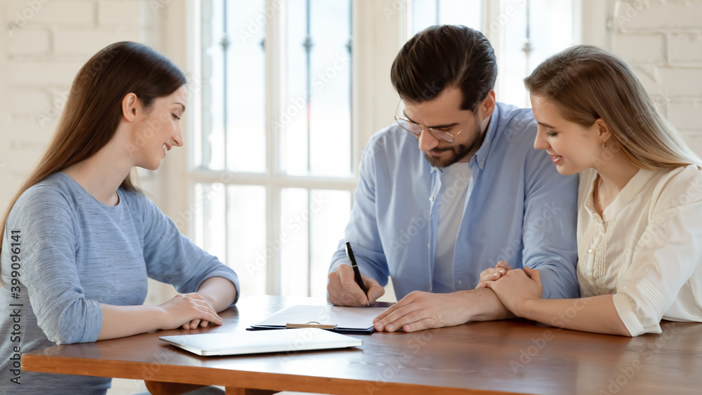 Wide banner view of happy young Caucasian couple sign paperwork close deal with real estate agent. Excited spouse renters put signature on document make agreement with realtor or broker at meeting. Wide banner view of happy young Caucasian couple sign paperwork close deal with real estate agent. Excited spouse renters put signature on document make agreement with realtor or broker at meeting.