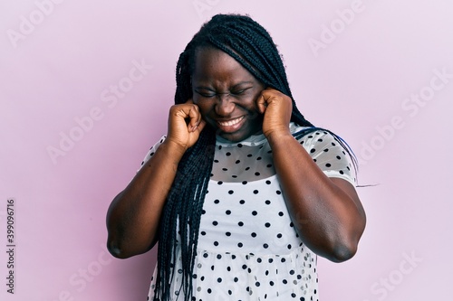 Young black woman with braids wearing casual clothes covering ears with fingers with annoyed expression for the noise of loud music. deaf concept. photo