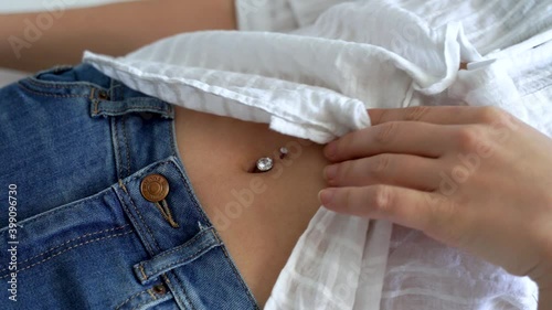 Young woman is showing her belly button or navel piercing isolated on white background.