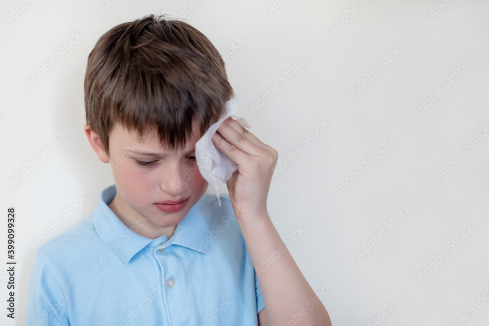 child in medical mask pressed handkerchief to head. boy with headache from a runny nose looks down sadly. child with flu, influenza or cold protected from viruses among patients with coronavirus child in medical mask pressed handkerchief to head. boy with headache from a runny nose looks down sadly. child with flu, influenza or cold protected from viruses among patients with coronavirus