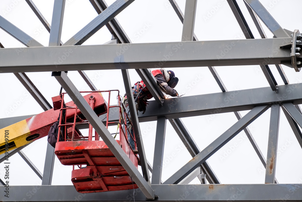 Man welder working on a crane performs high-rise work on welding metal structures of tower at a height. Man welder working on a crane performs high-rise work on welding metal structures of tower at a height.