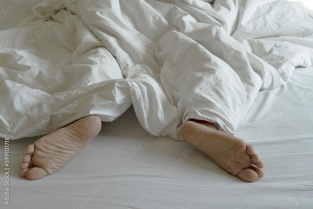 The feet or foot of couples sleeping on the bed and cover by the white blanket on a bright Sunday morning