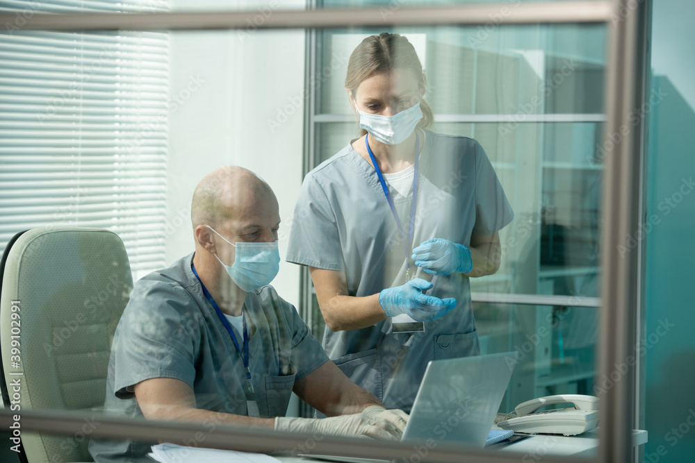 Obraz premium Young assistant or clinician in protective workwear pointing at laptop display