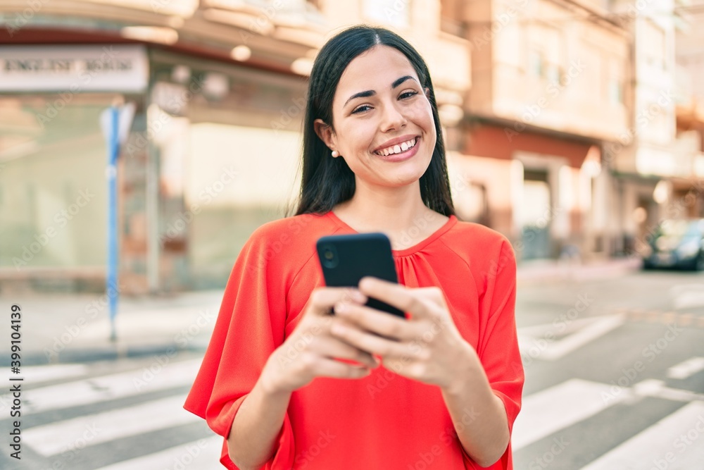 Young latin girl smiling happy using smartphone at the city.