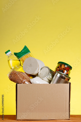 Food Donation concept. Donation Box With food For Donation On Yellow Backround. Assistance To The Elderly In The Context of The Coronavirus PandemicVertical shot.