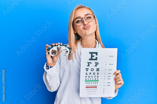 Beautiful caucasian optician woman holding optometry glasses and medical exam looking at the camera blowing a kiss being lovely and sexy. love expression.