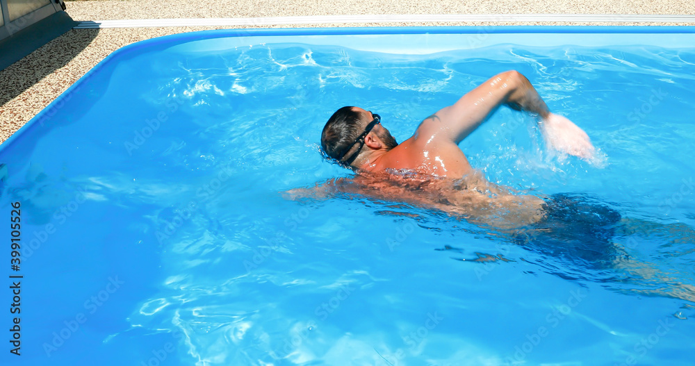 A young man trains in a home pool. Athlete swims in countercurrent. Fitness training as a healthy lifestyle.