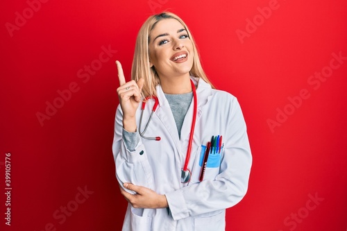 Young caucasian woman wearing doctor uniform and stethoscope with a big smile on face  pointing with hand and finger to the side looking at the camera.