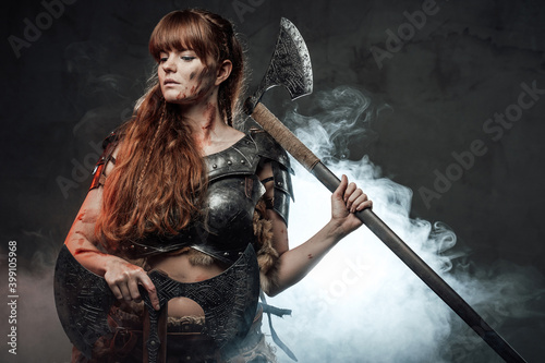 Violent and warlike northern woman warrior holding axes and posing in dark smokey background.