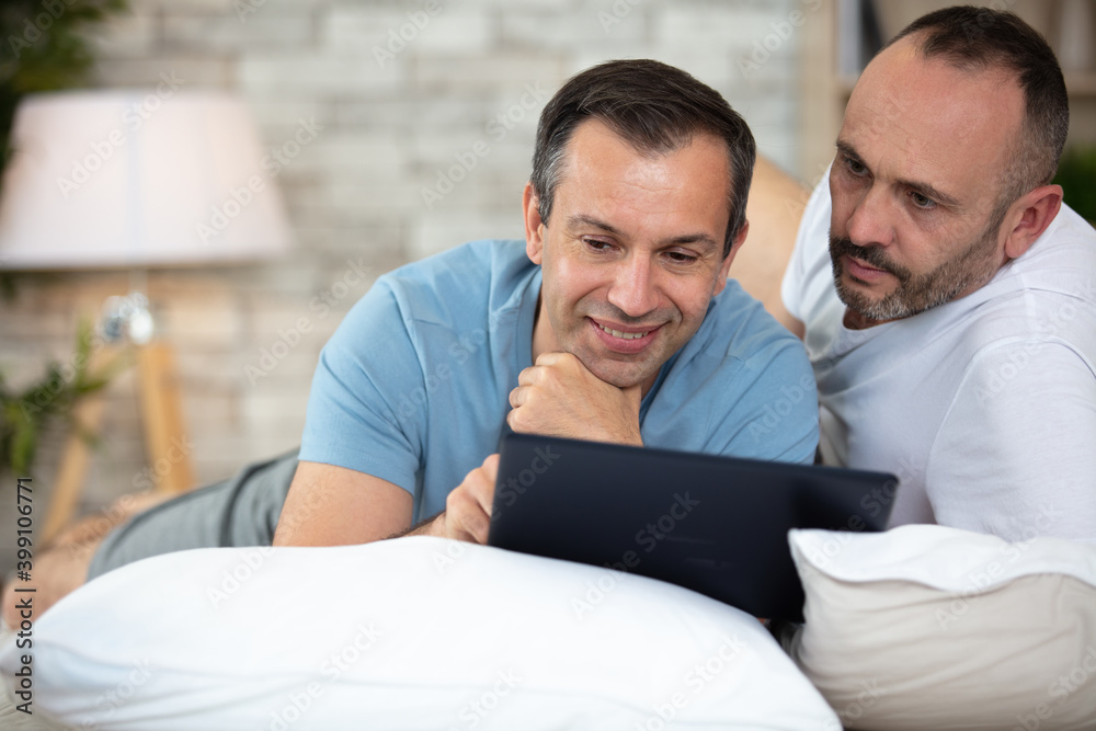 happy gay couple with tablet computer on bed at home happy gay couple with tablet computer on bed at home