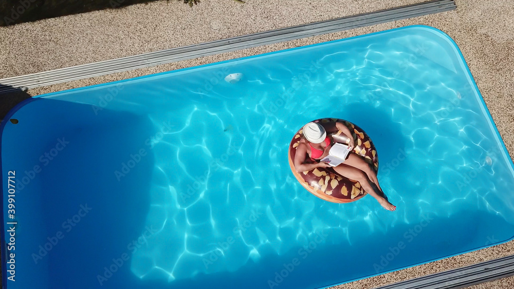 Young woman enjoying summer fun by the hotel pool. The girl relaxes with a book by the water. Wellness resort. Aerial view.