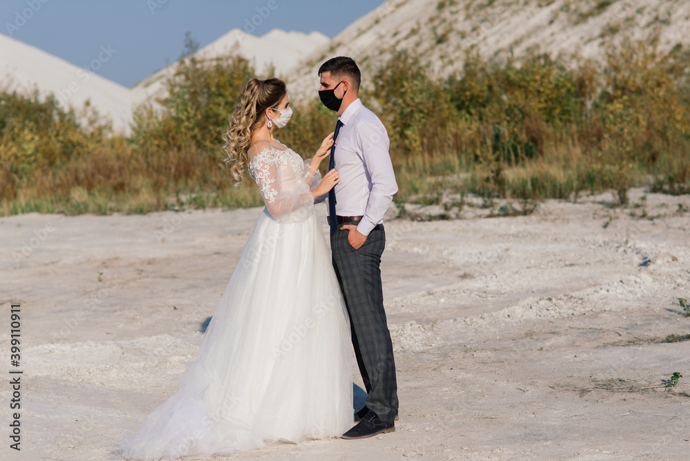 Young loving couple in medical masks in park during quarantine on wedding day. Young loving couple in medical masks in park during quarantine on wedding day.