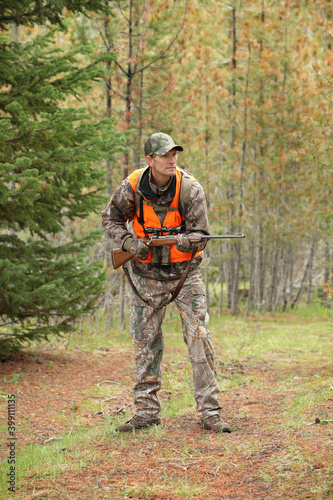 adult deer hunter sneaking through forest with rifle