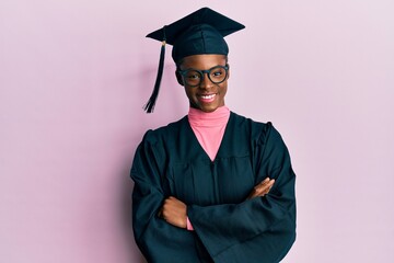 Young african american girl wearing graduation cap and ceremony robe happy face smiling with crossed arms looking at the camera. positive person.