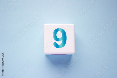 Close-up photo of a white plastic cube with a blue number 9 on a blue background. Object in the center of the photo