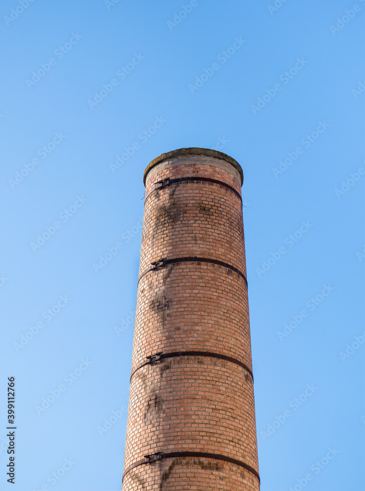 Old factory chimney made of red bricks against blue sky.