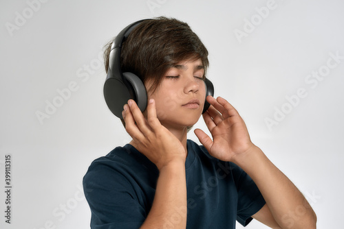 Portrait of little sportive boy child in sportswear wearing headphones, listening to music, standing with eyes closed isolated over white background