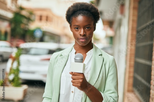 Young african american reporter woman with relaxed expression using microphone at the city