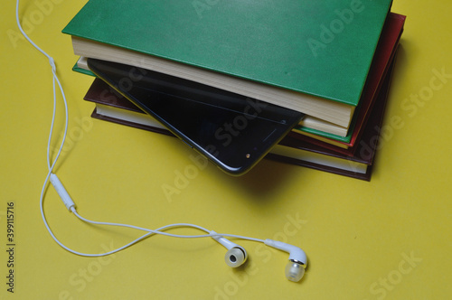 Headphones with books and a smartphone on a yellow background.