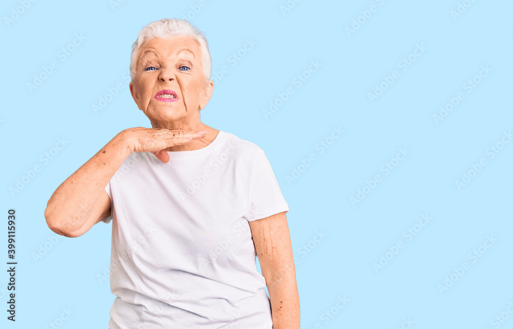 Senior beautiful woman with blue eyes and grey hair wearing casual white tshirt cutting throat with hand as knife, threaten aggression with furious violence Senior beautiful woman with blue eyes and grey hair wearing casual white tshirt cutting throat with hand as knife, threaten aggression with furious violence