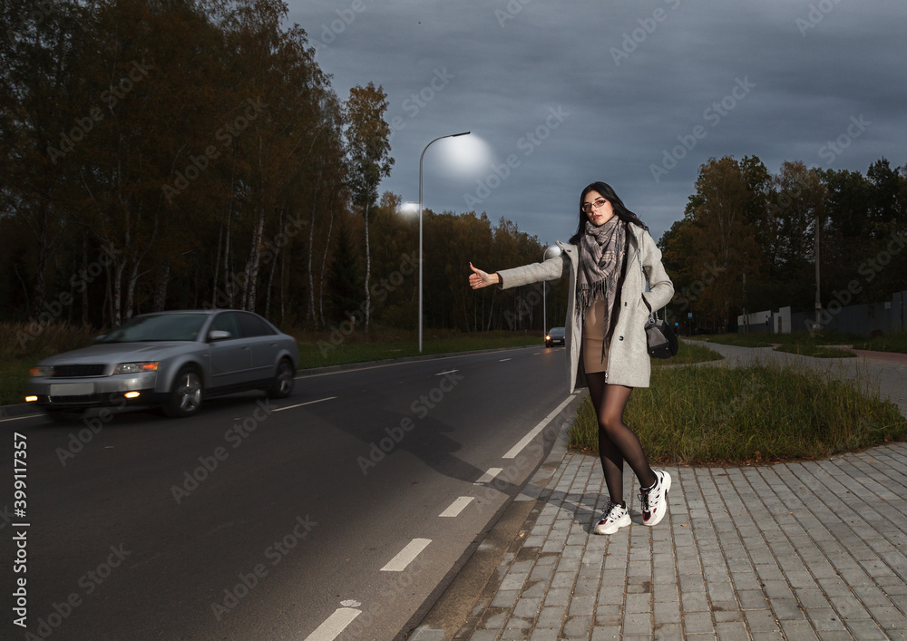 Fototapeta premium young girl in a gray coat stands near the road trying to stop a car