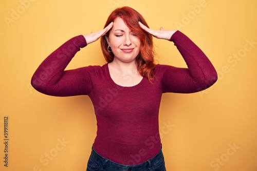 Young beautiful redhead woman wearing casual sweater standing over yellow background with hand on head, headache because stress. Suffering migraine.