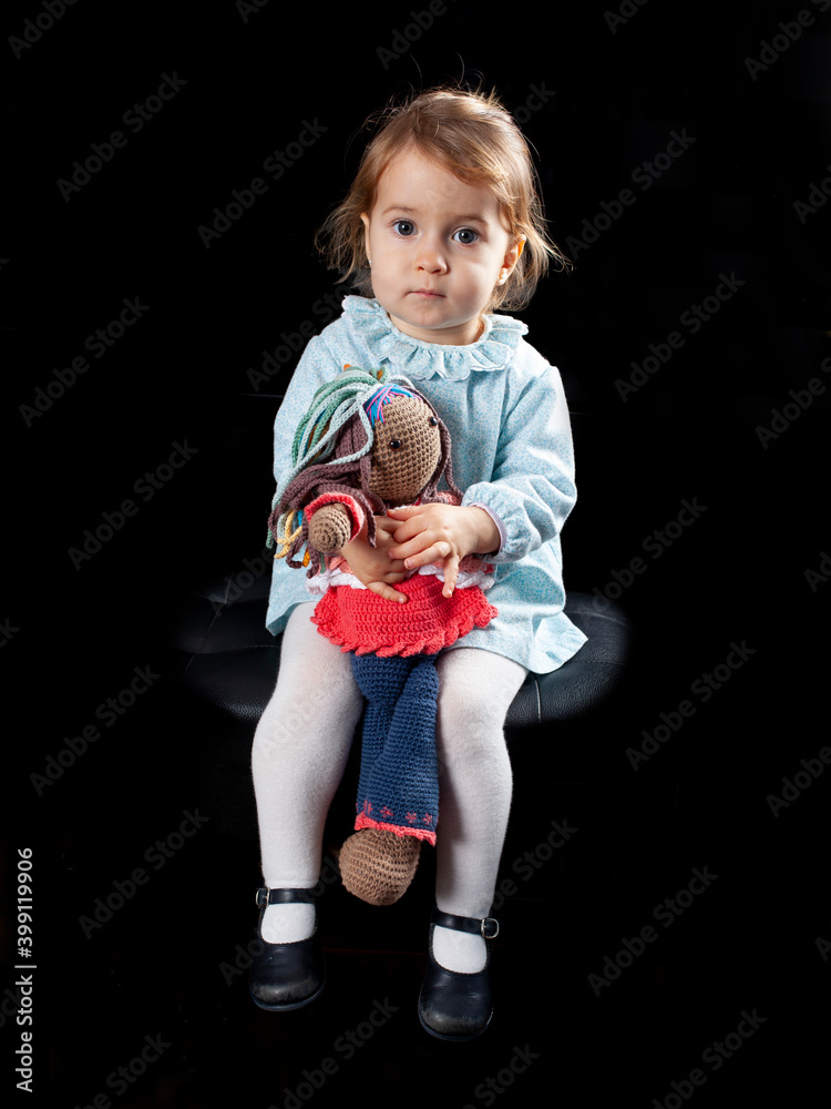 Niña pequeña con muñeca de trapo sentada sobre fondo negro