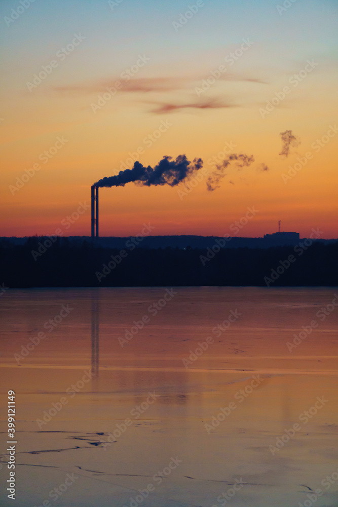 Vertical double chimney with puffs of smoke against the backdrop of a magnificent sunset