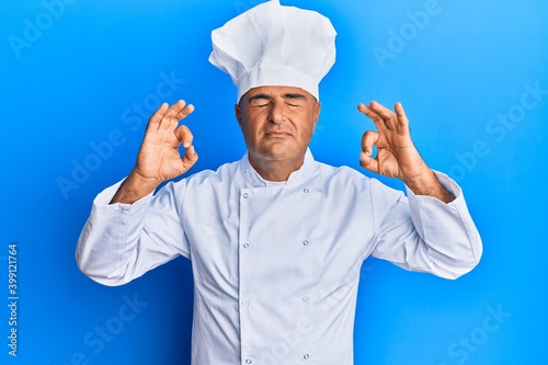 Mature middle east man wearing professional cook uniform and hat relax and smiling with eyes closed doing meditation gesture with fingers. yoga concept.