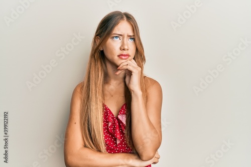 Beautiful young blonde woman wearing summer dress thinking concentrated about doubt with finger on chin and looking up wondering
