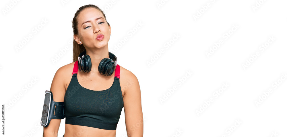 Beautiful blonde woman wearing gym clothes and using headphones looking at the camera blowing a kiss on air being lovely and sexy. love expression. Beautiful blonde woman wearing gym clothes and using headphones looking at the camera blowing a kiss on air being lovely and sexy. love expression.