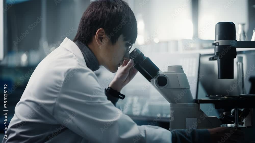 Medical Development Laboratory: Portrait of East Asian Scientist Looking Under Microscope, Analyzes Petri Dish Sample. Big Pharmaceutical Lab doing Medicine, Biotechnology, Microbiology,Drugs Research