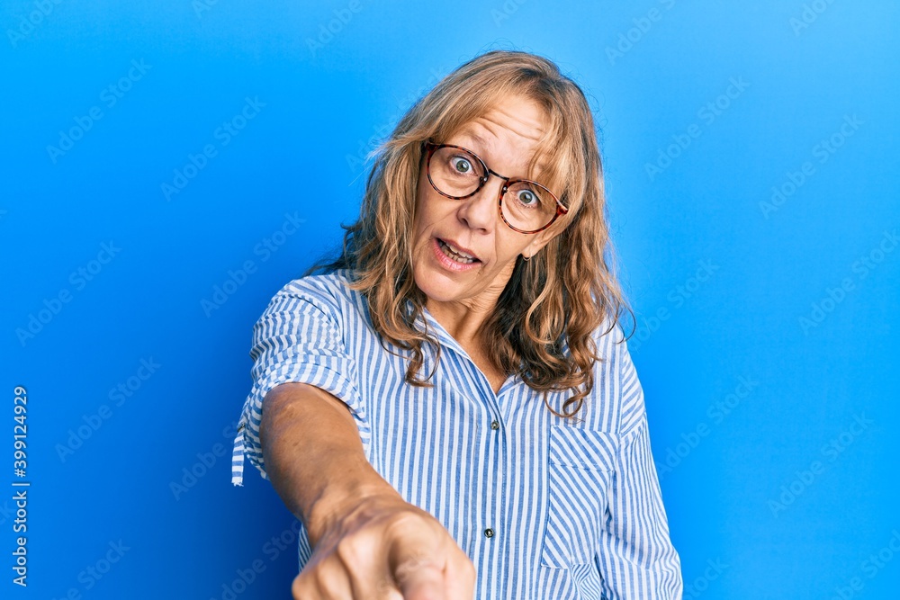 Middle age blonde woman wearing casual clothes and glasses pointing displeased and frustrated to the camera, angry and furious with you Middle age blonde woman wearing casual clothes and glasses pointing displeased and frustrated to the camera, angry and furious with you