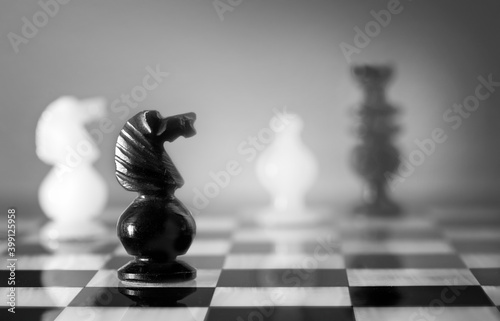 Primer plano de un caballo negro de ajedrez en un tablero de alabastro y con varias figuras de fondo un tanto desenfocaras.